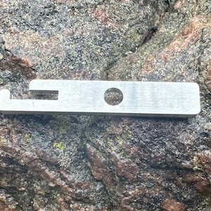 以下が含まれることがあります： 片側に穴とフックが付いた銀色の金属製のツール。このツールは、アイテムを開閉するために設計されています。