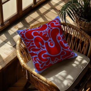 May include: A blue and red patterned cushion with a whimsical design. The cushion is sitting on a wicker chair.