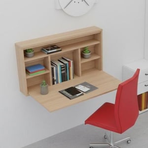 Könnte beinhalten: Ein modernes Heimbüro mit einem an der Wand befestigten Holzschreibtisch, einem roten Stuhl und einem großen weißen Regal mit Ordnern und Büchern. Eine weiße Uhr hängt an der Wand. Der Schreibtisch hat eine herunterklappbare Arbeitsfläche.