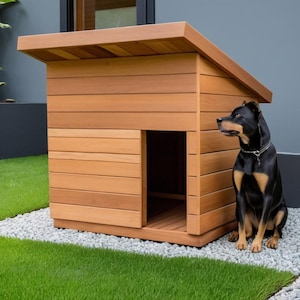 May include: A wooden dog house with a sloped roof and an open doorway. A black and brown dog sits on a bed of small white stones next to the house. The dog house is made of light brown wood.