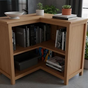 May include: A light oak corner bookshelf with multiple shelves filled with books. The top surface holds a white bowl, small potted plants, and books. The bookshelf is in a modern living space with a concrete floor and large windows.