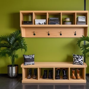 May include: A wooden entryway bench with storage shelves and hooks. The bench has a light wood finish and is decorated with two throw pillows, two potted plants, and a framed print of a leaf.
