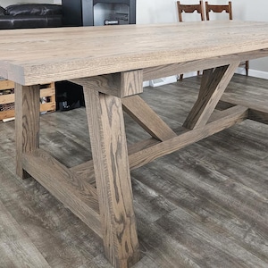May include: A rustic wooden dining table with a gray stain finish. The table has a rectangular top and a unique X-shaped base.