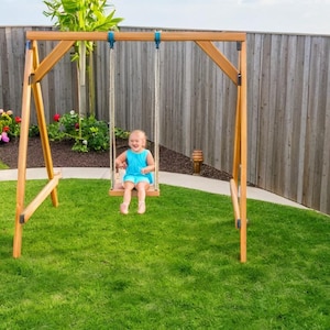 Op de afbeelding: Een houten schommelset met een kind dat op een blauwe schommel zit. De schommelset staat in een achtertuin met een houten hek en groen gras.