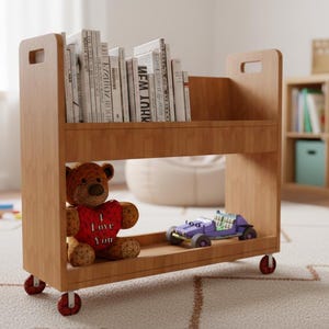 Peut inclure: Une étagère en bois brun clair sur roulettes, remplie de livres. Un ours en peluche avec un cœur rouge et une voiture jouet violette sont sur l'étagère inférieure. L'étagère a une poignée de chaque côté.