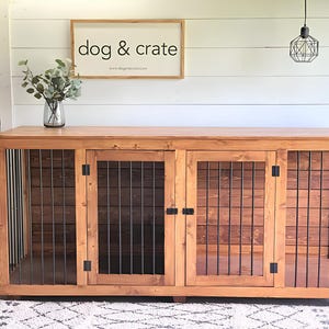 May include: A wooden dog crate with two doors and a metal grate. The crate is stained a dark brown color and has black metal hinges. The crate is sitting on a white rug in front of a white wall.