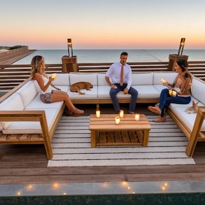 May include: A white sectional sofa with white cushions sits on a wooden deck overlooking the ocean. The sofa is decorated with throw pillows and a small coffee table with candles.