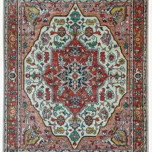 Puede incluir: Una alfombra rectangular con un diseño intrincado y simétrico. La alfombra presenta un medallón central en tonos rojos, turquesas y crema, rodeado por un borde de patrones florales repetidos en colores similares. La paleta de colores de la alfombra es cálida, con una estética vintage.