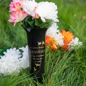 Könnte beinhalten: Schwarze Keramikvase mit goldener Aufschrift "In Loving Memory GRANDAD A True Gentleman We miss you so much". Die Vase ist mit rosa und weißen Blumen gefüllt und steht auf grünem Gras.