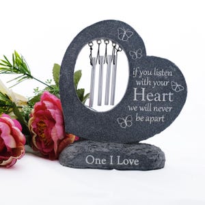May include: A grey stone heart-shaped wind chime with the text "if you listen with your Heart we will never be apart" and "One I Love". The wind chime has silver chimes and butterfly accents. Pink and yellow flowers are in the background.