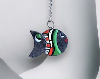 Può includere: Una collana con catena d'argento con un ciondolo a forma di pesce nero, verde, rosso e bianco. Il pesce ha un design stilizzato ed è dipinto con colori vivaci.