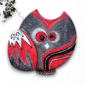 May include: A decorative owl figurine with a red, black, and white color scheme. The owl has large, round eyes and a textured surface. The design features a combination of geometric and organic shapes, creating a unique and artistic appearance.