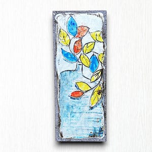 May include: A ceramic tile with a hand-painted design of a blue vase with yellow, blue, and red leaves. The tile has a textured, gray border.