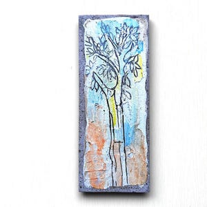 May include: A hand-painted ceramic tile with a blue, yellow, and orange background. A black line drawing of a tree with leaves is in the center of the tile.