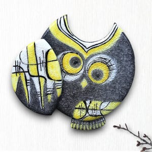 May include: A ceramic owl figurine with a cracked glaze finish. The owl is primarily gray and yellow, with white accents around the eyes and on the separate wing piece. The design features geometric patterns and a stylized appearance.