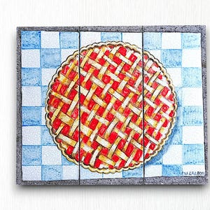 Op de afbeelding: Een handgeschilderde keramische tegel met een rode en gele taart op een blauw-wit geblokte achtergrond. De tegel is gesigneerd met "Emma Lana Rooke".