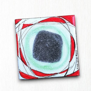 Könnte beinhalten: Eine weiße quadratische Fliese mit einem abstrakten Design in Rot, Schwarz und Grün. Das Design zeigt einen schwarzen Kreis mit einem grünen Ring darum, umgeben von roten Linien. Die Fliese ist signiert mit "Etna Cave Rock".