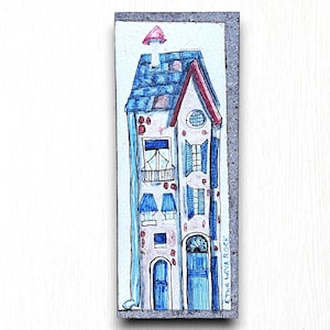 May include: A hand-painted ceramic tile depicting a colorful, multi-story building with blue shutters and a red roof. The tile is framed in a gray border and has the text "Etna Lava Rock" written vertically on the right side.