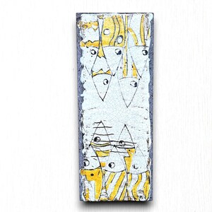 May include: A white ceramic tile with a blue border and a design of yellow and white fish. The fish are arranged in a vertical pattern and have simple black eyes.