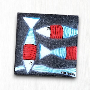 Könnte beinhalten: Drei stilisierte Fische, die auf eine schwarze quadratische Fliese gemalt sind. Die Fische sind weiß mit roten und blauen Streifen. Die Fliese ist unten rechts mit "Etna Cavaroc" signiert.