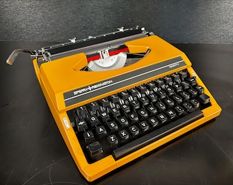 Máquina de escribir Sperry Remington Tenfifty antigua, color amarillo ocre, revisada y limpiada, en perfecto estado de funcionamiento, con estuche y cinta bicolor.