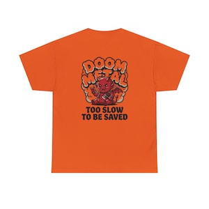 Peut inclure: Un t-shirt orange à manches courtes avec un motif représentant un petit diable rouge tenant une hache. Le texte au-dessus du diable indique DOOM METAL, et le texte en dessous indique TOO SLOW TO BE SAVED. Le motif est centré au dos du t-shirt.