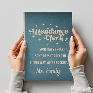 May include: A teal-colored notebook with the words "Attendance Clerk" in a retro font. The notebook includes the phrases "SOME DAYS I ROCK IT. SOME DAYS IT ROCKS ME. EITHER WAY WE'RE ROCKIN'. Ms. Emily."