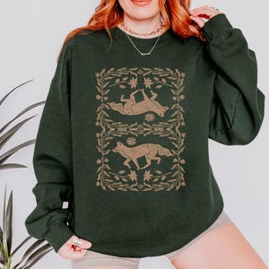 May include: A dark green sweatshirt with a graphic print of two foxes in a floral design. The foxes are in a light brown color.