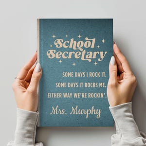 May include: A teal notebook with the words "School Secretary" in a retro font. The notebook has the text "Some days I rock it. Some days it rocks me. Either way we're rockin'. Mrs. Murphy."