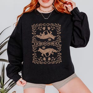 May include: Black sweatshirt with a graphic print of two stylized foxes in a floral frame. The foxes are brown and the frame is a light brown color.