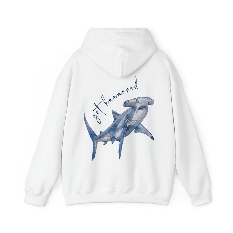 May include: White hoodie featuring a watercolor hammerhead shark illustration in shades of blue and gray. The text "get hammered" is written above the shark in a cursive font. The hoodie has a hood and long sleeves.