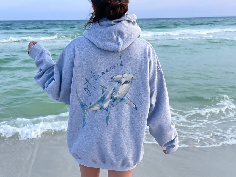 May include: A gray hooded sweatshirt with a blue hammerhead shark and the text 'get hammered' printed on the back.