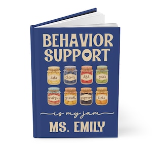 May include: A navy blue journal with the words "BEHAVIOR SUPPORT" in white. The journal features illustrations of jars with labels like "data" and "charts." The text "is my jam" and "MS. EMILY" are also visible.