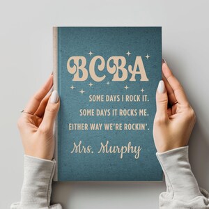 May include: A teal notebook with the text "BCBA" in a retro font, along with the phrases "Some days I rock it," "Some days it rocks me," and "Either way we're rockin'." The name "Mrs. Murphy" is also included.
