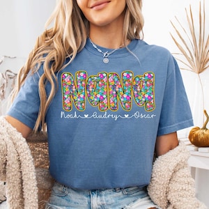 May include: A blue t-shirt with a floral design that spells out "NANA" with the names "Noah, Audrey, Oscar" underneath.
