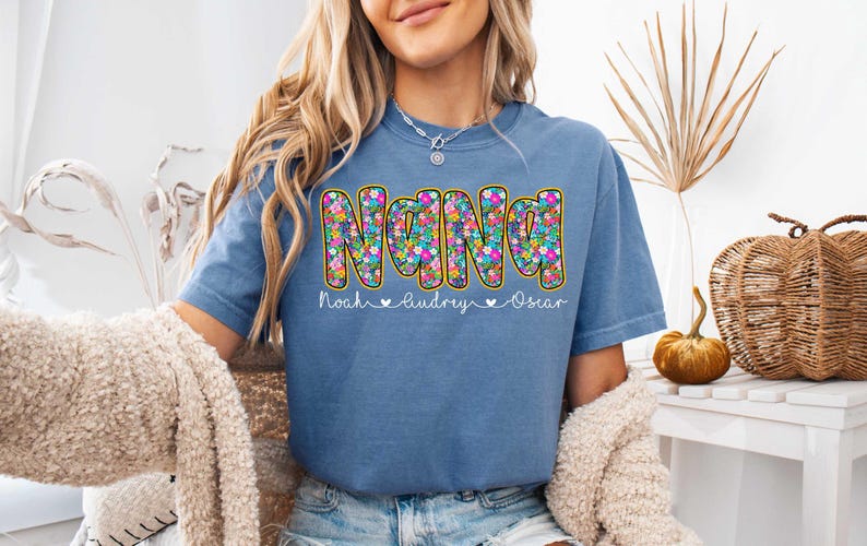 May include: A blue t-shirt with a floral design that spells out "NANA" with the names "Noah, Audrey, Oscar" underneath.