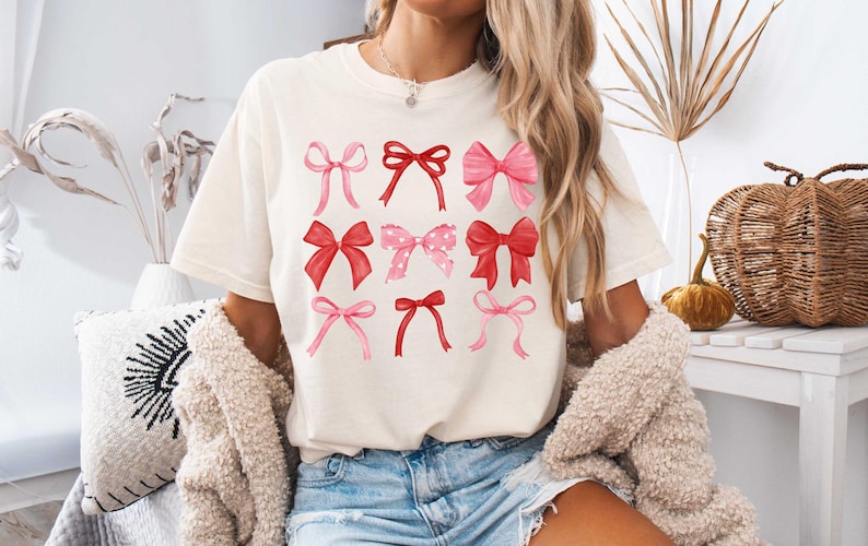May include: A white t-shirt with a graphic of pink and red bows. The bows are arranged in a grid pattern on the shirt.