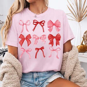 May include: A pink t-shirt with a graphic of nine red and pink bows. The bows are arranged in three rows of three.