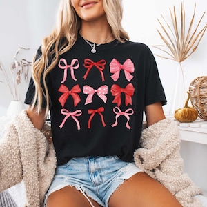 May include: A black t-shirt with a graphic of pink and red bows. The bows are arranged in a grid pattern.