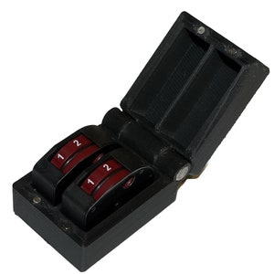 May include: A black plastic box with a hinged lid, revealing two red and black numbered dials. The dials are labeled with the numbers "1" and "2".