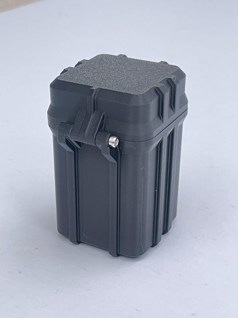 May include: A black, square-shaped, plastic storage container with a textured lid and a latch.