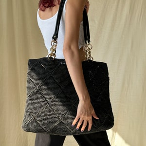 Pode incluir: Uma bolsa tote de crochê preta com alças de couro preto e detalhes de corrente dourada. A bolsa tem um padrão de diamante e é grande o suficiente para carregar os itens essenciais do dia a dia.