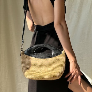 May include: A black and tan woven bag with a black leather handle. The bag is worn by a person wearing a black backless dress.