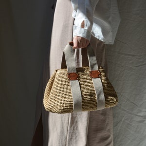 A beige handmade crochet raffia purse bag with a woven-style texture, brown leather accents, thick beige fabric handles, and a lightweight bohemian summer style for casual everyday outfits.