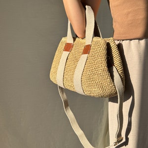 May include: A beige handmade crochet raffia purse bag with a woven-style crochet texture, brown leather accents, beige fabric handles, and a long adjustable strap.