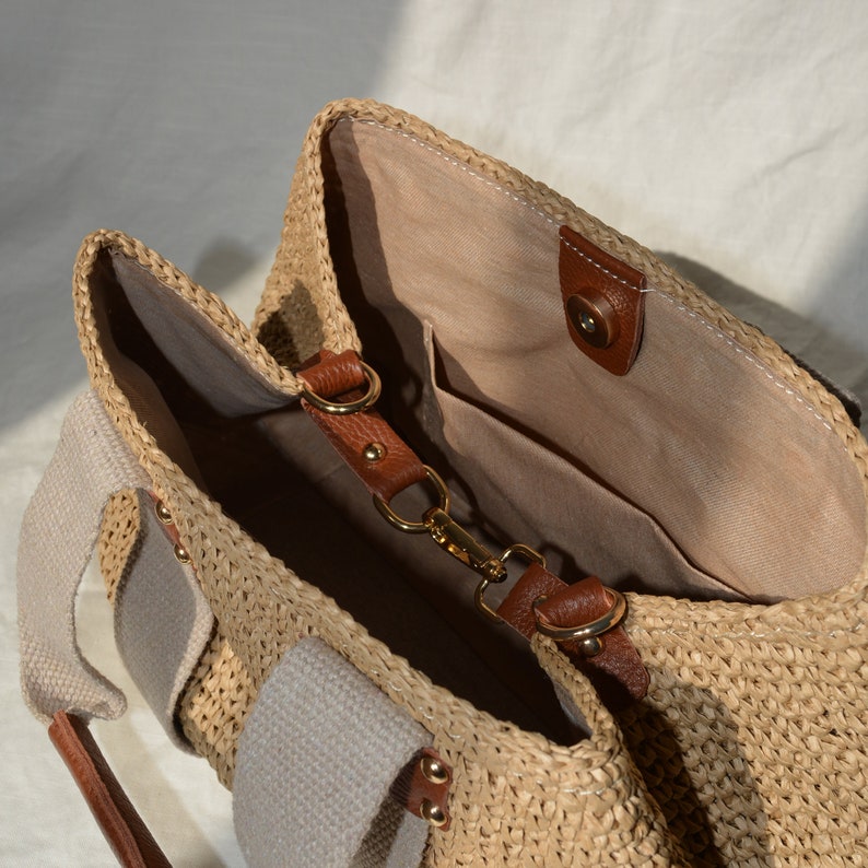 May include: A handmade crochet raffia purse bag with beige canvas lining, brown leather strap details, inner pocket, and natural boho summer style. A lightweight handmade raffia handbag for casual, beach, and everyday outfits.