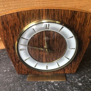 Peut inclure: Une horloge vintage en bois avec un cadran blanc et des aiguilles dorées. L'horloge a un design unique et incurvé et une base en laiton.