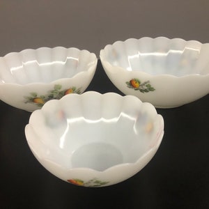 May include: Three white ceramic bowls with scalloped edges and a floral design featuring apples and leaves. The bowls are nested together, with the largest bowl on the bottom and the smallest bowl on top.