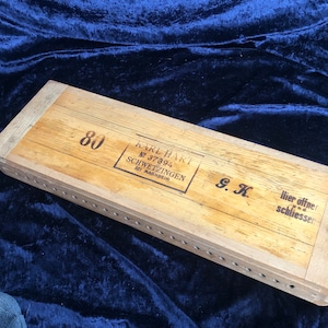 Pode incluir: Uma caixa de madeira com o texto "Karl Hart No 37894 Schwetzingen bei Mannheim G.K. Hier offner und schliessen" impresso na parte superior. A caixa está etiquetada com o número "80".