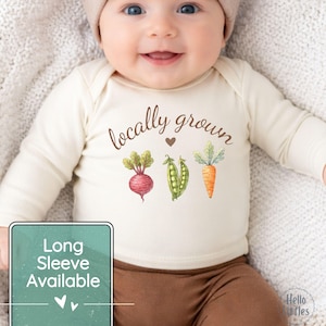 May include: A cream-colored long-sleeve baby bodysuit with the words "locally grown" and a heart graphic. Below the text are watercolor illustrations of a beet, peas, and a carrot. A green rectangle with the text "Long Sleeve Available" is in the lower left.